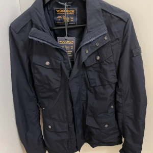 Woolrich jacka - Säljer denna asfeta woolrich jacka med prislapparna kvar, skick: 10/10! Den är i strl S men passar M och är verkligen den perfekta sommar/höst jackan! Nypris ligger på omkring 3000 men mitt pris bara 1299kr! Hör av er🫡