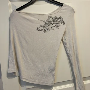 Vit enärmad tröja med tryck - Fin enärmad tröja som har tryck på en ängel. Använd få gånger. Väldigt skönt material. För fler frågor är det bara att skriva till mig!😊