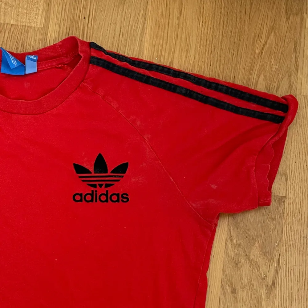 Röd adidastshirt med svarta detaljer, själva märket är i typ plysch? I bra skick, ränderna är möjligen en aning bleka.. T-shirts.