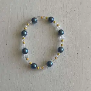 Ett egengjort pärlarmband med färgeren blå, vit och gul med en blandning pärlsorter. 