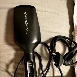 Svart hårborste med sladd från Björn Axén Tools - En svart elektrisk hårborste från Björn Axén Tools, designad för att användas med sladd. Borsten har en ergonomisk design och är utrustad med en strömbrytare och temperaturkontroll. Den är idealisk för att styla och torka håret samtidigt.
