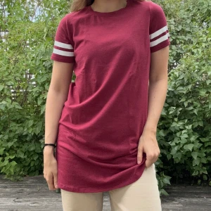 Lång vinröd T-shirt/T-shirtklänning - Lång, cool och stretchig t-shirt/ t-shirtklänninh med vita ”gummi”texturerade ränder på båda armarna från Forever 21. Storlek: S. Material: 57% bomull + 38% polyester + 5% elastan. :)