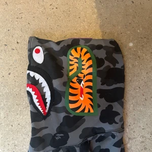 Grå Bape fullzip Hoodie  - Snygg bapehoodie som är använd Max 5 gånger. Säljer för är inte min stil längre. Skick 9/10 då det är lite problem med zippern.🔥Stoleken är L men passar mer som M. Påsen till hoodien kommer med!!! Skriv gärna för fler bilder!