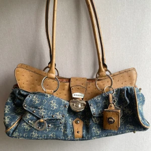 Vintage guess väska  - Vintage guess denim väska! Mellan stor, finns 3 extra små fack inuti, ett fack i bak som stängs med dragkedja, 2st i fram. Ingår även en nyckelring som går att öppna och lägga in en liten personlig bild i 💞