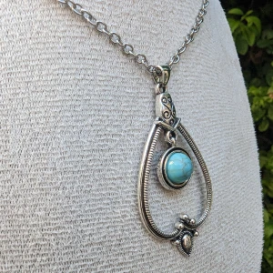 Vintagestil Halsband i Antikt Silverfärg med Geometriskt Hänge - Säljer ett elegant halsband i vintagestil med en antikt silverfärgad finish. Halsbandet har ett geometriskt hänge som pryds med en turkos och strassdekor, vilket ger det en unik och lyxig känsla. Det är helt oanvänt och i perfekt skick.