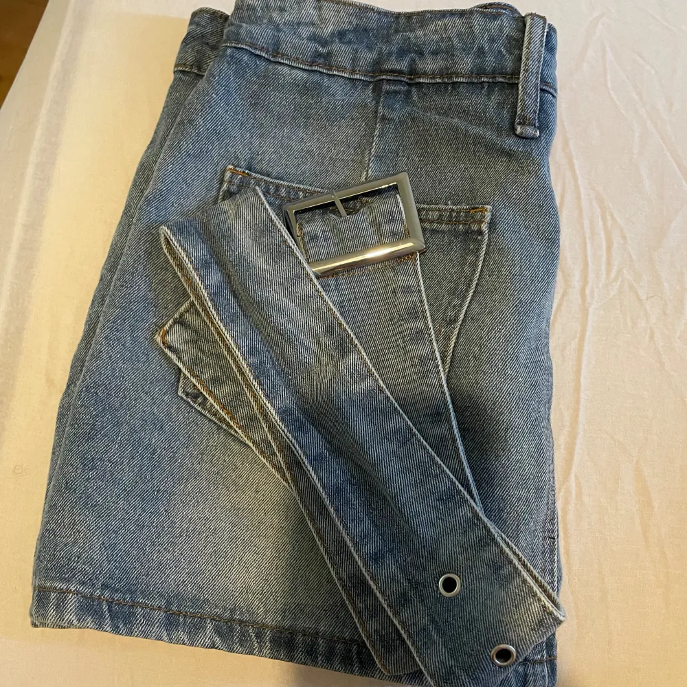 En kort jeanskjol med skärp. Säljs då den är för liten för mig.. Den är helt ny, aldrig använd. Det är stl L men är väldigt liten i stl, sitter som en S/M.  Den har bekväma och inbyggda shorts under så man inte råkar visa onönskade delar😊Nypris 229kr. Kjolar.