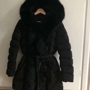 Vinterjacka - Jag säljer min svarta vinterjacka i dun och äkta päls med ett svart läder bälte till.  Använd 2 vintrar men är i bra skick. Ett lagat hål i vänster ficka som inte syns eller känns och en mindre lagning inne i fodret. Storleken fungerar med S.