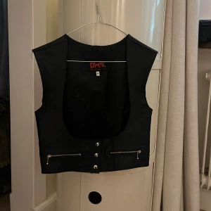 Läder korsett - Svart läder corsett/väst. Knappar fram och bak, går att justera i storlek. Jag bär i vanliga fall S/36 och denna M fungerar bra. Märke är Demask och plagget är i fint skick. Har du några frågor eller vill se mer bilder är det bara att skriva :)