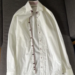 Bugatti vit skjorta - Vit bugattiskjorta med röda knappar och detaljer. Sparsamt använd. Kostade runt 1000 ny. Storlek 38 passar främst small men kan passa medium.