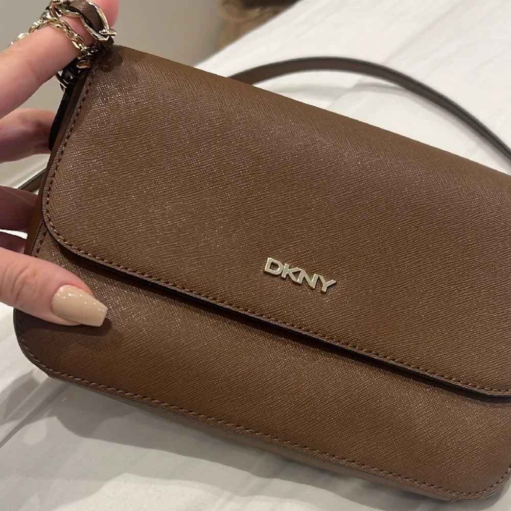 DKNY väska i nyskick. Väskan är brun med guldtetaljer. . Väskor.