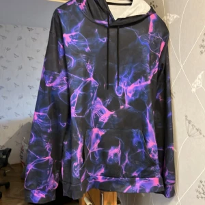 Multifärgad hoodie - Riktigt snygg hoodie i nyanserna lila/svart och rosa. Bekväm att ha på sig. Tyvärr så passade den inte mig så den är aldrig använd. Den har snören och magficka