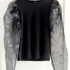 Fest-topp med meshärmar  - Festlig topp från Gina Tricot i storlek M.   Mesh-ärmar med puffaxlar och otroligt bekvämt material på resten av tröjan. Något stretchigt och lätt på kroppen.   Fint skick! 