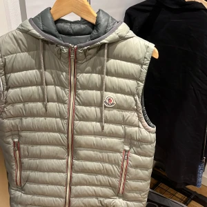 Moncler väst - Moncler väst i använt skick Riktigt fräsch med luva nu inför våren/sommarn Defekter: flaw vid märket och ett fixat liten flaw. Lite water stains men inget som syns direkt  Vid snabb affär kan jag tänka mig gå ner i pris SJÄLVKLART ÄKTA