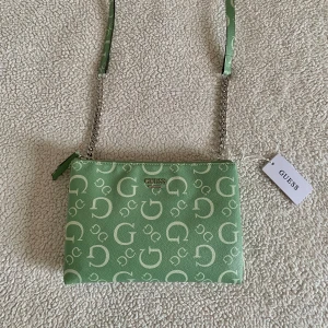 Guess Valence axelremsväska - Otroligt vacker axelremsväska från Guess med klassisk ”G”-logo mönster. Två stora fack och mindre kortfack innanför. Ordinariepris 1300kr.