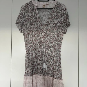 Blommig klänning H&M, 38 - Mycket söt liten klänning från H&M i storlek 38. Klänningen är mycket god skick.   Material: 100% viskos  Mått: Längd ca 85 cm Byst ca 50 cm Midja ca 35-60 cm (elastisk, man kan även dra åt)  Plagget kommer från ett djur- och rökfritt hem. 