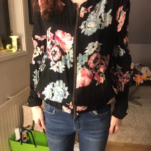 Blommig kofta - En svart kofta med rosa blommor och gröna löv 