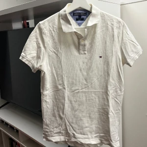 Tommy Hilfiger Piké vit - Säljer denna snygga piké från Tommy Hilfiger då den är lite för liten för mig. / Bra skick, dock är den lite lite missfärgad under armhålan men inget man tänker på. Se bild 3! / Storlek S
