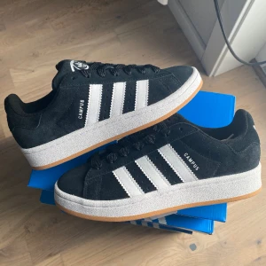Adidas Campus 00s ”Black White Gum” - Säljer dessa svarta Adidas Campus 00s ”Black White Gum”. De är helt nya och oanvända. Köpta ifrån Zalando och självklart äkta. Finns i storlek 38. Betalning sker genom Swish till vår företagsswish och paketet skickas spårbart samma dag.