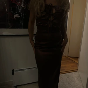 Brun ärmlös klänning - Mörkbrun elegant Maxi klänning med dragkedja. Aldrig använd. Satin. Passar i XS som tjejen på bilden. Passar otroligt bra till en fest
