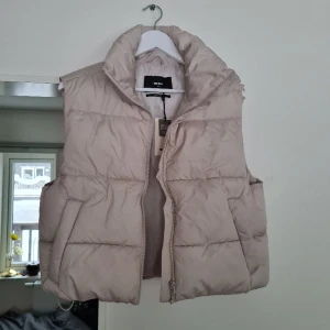Väst, puffer vest - Offwhite väst, dragkedja och dragsko på båda sidorna nertill på insidan. Finns ett litet litet hål på baksidan men inget som syns märkvärdigt. Helt oanvänd, prislapp kvar, nypris: 399:-.  Material: 50% Återvunnen Polyester, 50% Polyester. 