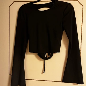 Svart festtopp - Superfin svart croppad topp med trumpetärmar och snörad rygg.  Jättefina detaljer och tyget känns lyxigt!  Endast använd några gånger så jättefin kvalite!  Skriv vid fler bilder eller intresse!🖤