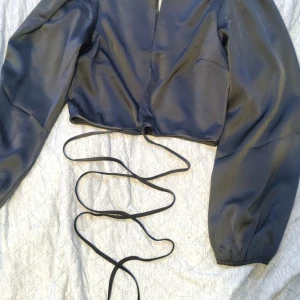 Klar för fest! - En svart silkes topp. Långärmad, liten högre krage, fin öppning i mitten av bysten även snörning ner runt magen och perfect till fest. Helt oanvänd (lappen är kvar)💗