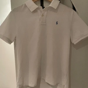 Ralph Lauren piké - Säljer en Ralph Lauren piké i bra skick förrutom en knapp som lossnat längst upp, men inget som märks. Den är vit med en ljusblå logga. Tröjan är stor i storleken och passar runt 170. Vid frågor är det bara att höra av sig!