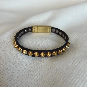 Edblad nitarmband - Armband från Edblad i brunt läder med nitar i blank 14K guldplätering på rostfritt stål (nickelsäkert). Köpt för 499 kr och i nyskick förutom att en av nitarna har ramlat av (se bild 4) och några knappt märkbara/ pyttesmå repor på magnet låset.