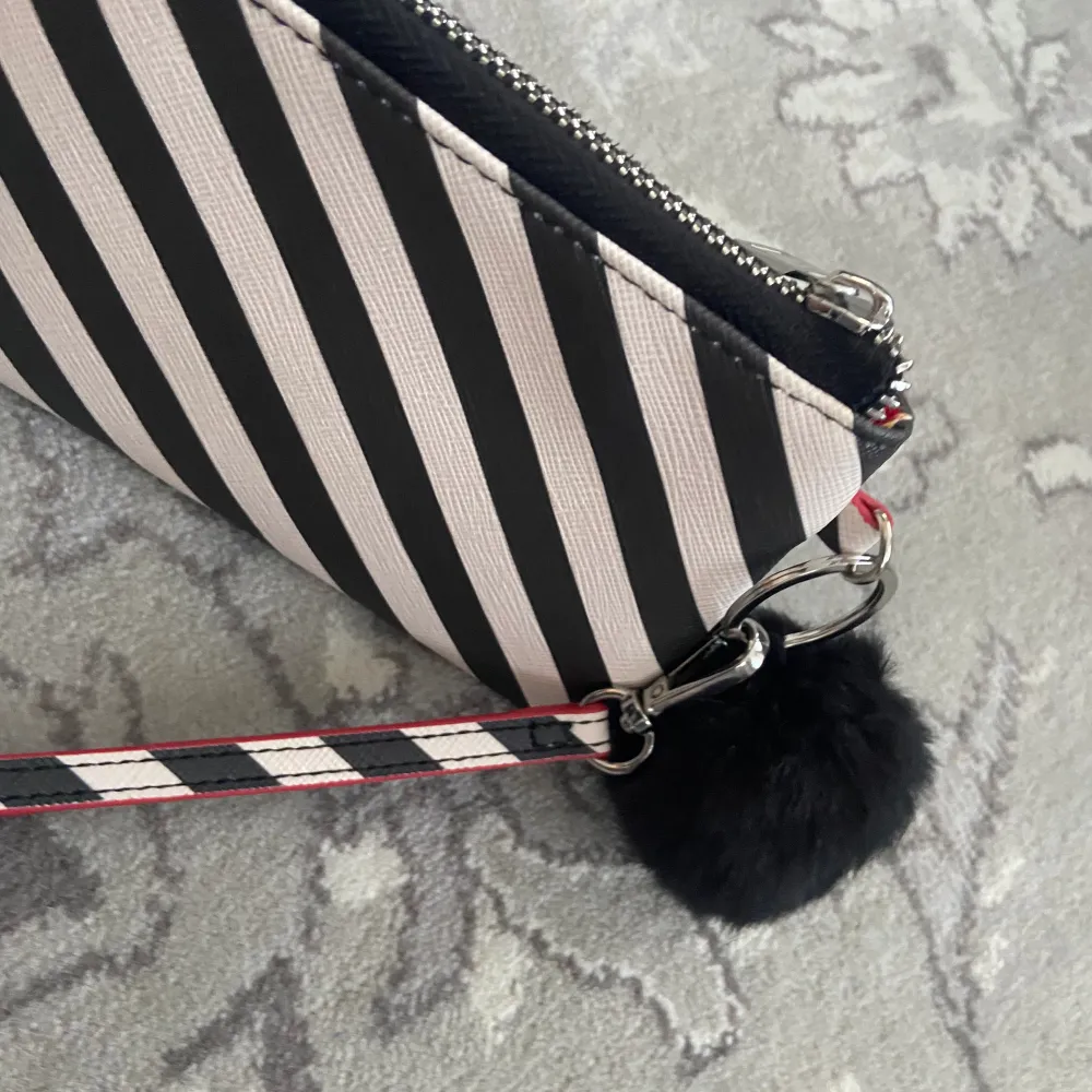 Plånbok med zebra mönster röd i insidan med en svart fluffboll som hänger på utsidan som dekoration . Asusteet.