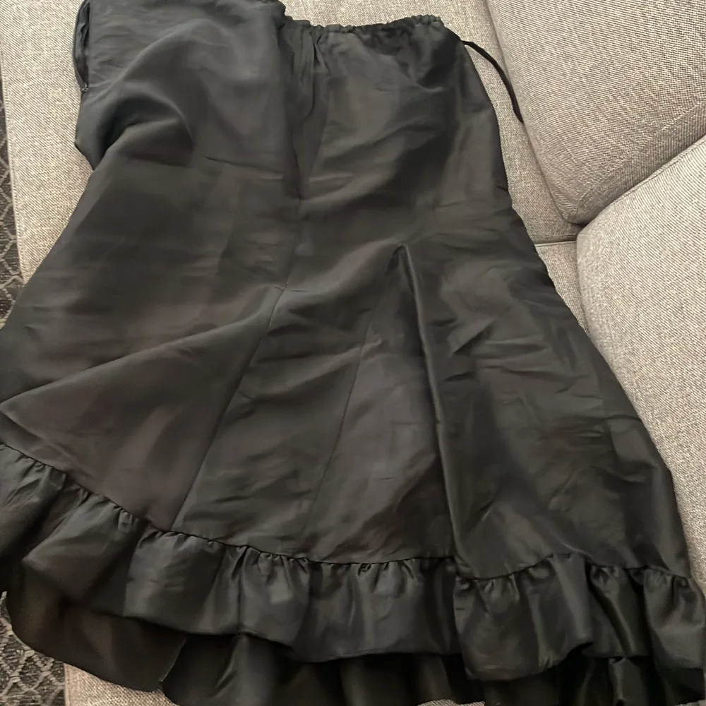 En lång svart kjol med luftigt skönt material och en dragkedja på sidan. Passformen och längden är reglerbar med ett snöre på sidan. Den är köpt second hand för några år sedan men aldrig använd för den är för liten. Skulle  säga att den passar M - L.. Kjolar.