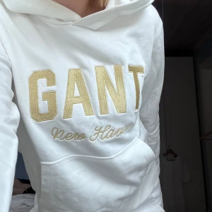 Gant hoodie - Vit gant hoodie med guldskimrande motiv. Mer som vanlig tröja i materialet men med huva. Nyskick, barn storlek 170/15yo men passar XS lika bra.