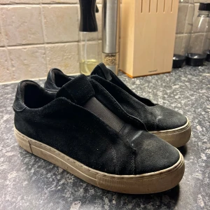Svarta sneakers från Axel Arigato - Ett par svarta sneakers från Axel Arigato i mocka. Skorna har en vit sula och är i välanvänt skick. *Skrivet av AI. Men inte mycket mer att säga, välanvända axel arigatos. Bor ute på landet så dom har fått stå ut. Men dom är hela och med an tvätt så ser dom nog väldigt mycket bättre ut. Kan tvättas vid köp. Strl 39, nypris 2550 på NK. Modellen heter 360 laceless🤠Hör gärna av dig vid frågor eller intresse