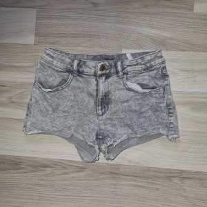 Grå jeansshorts - Ett par grå jeansshorts med hög midja. Shortsen har en knapp och dragkedja framtill samt två framfickor och två bakfickor. De har en sliten look med fransiga kanter. Från H&M i stl 146.