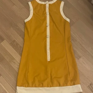 60- tals klänning - En väldigt retro klänning från märket Pop. Fin senapsgul färg, med vita detaljer. Klänningen visar tydliga tecken på användning, men är i gott skick. 