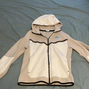 Vit Nike tech fleece - Säljer en Nike tech fleece som är köpt för ungefär 1 år sedan från deras egen hemsida. Storleken är s men passar även m. Den har några fläckar på ena ärmen så därför säljer jag den billigt. Skick 7/10 skriv vid några funderingar