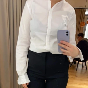 Holly & Whyte gullig blus - Supergullig vit blus från Holly&Whyte i storlek 40. Blusen har söta knappar och volang på krage och ärmar. Blusen är sparsamt använt i gott skick och jag säljer eftersom den tyvärr blivit för stor.