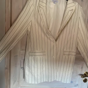 Vit randig kavaj  - Vit randig kavaj med axelkuddar   Använd 1 gång  2 riktiga fickor fram   Stl 40