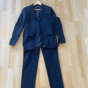 svart kostym, kavaj och kostym byxor från Jack and Jones - Svart kostym size 46 och superslim från Jack and Jones. Helt nyskick, använt en gång på balen i nian för två år sedan. Hör av dig om du har frågor ✌️