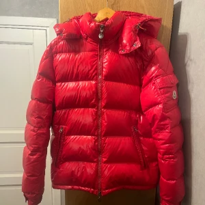 Moncler Maya Jacka (röd) - En Moncler Maya jacka av den äldre modellen i super fint skick! Jackan säljer jag då den inte använts på ett år. Detta är en äkta jacka köpt av Garmsmarket! Går naturligtvis att checka koden i jackan! Väldigt bra skick, endast cartoonen som gått av.  9/10