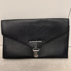 Svart väska - Svart kuvertväska från Calvin Klein jeans!  - blå inuti  - ca 28 cm bred  - ca 17 cm hög Använd några enstaka gånger, i gott sick.