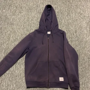 Luvtröja  - En begagnad luvtröja. Färg mörkblå men den skimrar lite i färgen. Se bilder. Är så över hela tröjan så kan inte tänka mig att det är fläckar. Lite små noppig också. Syns också på bilden. Men en superskön tröja 😁 Kommer från ett djur och rökfritt hem.