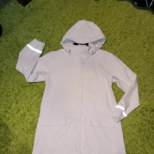 Regnrock Holly & Whyte - Regnrock i vit galon från Holly & Whyte. Fint skick, men svagt färgad (av en tidigare galge) på insidan. Syns inte vid användning. 