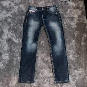 Tvär feta jeans med riktigt tuff fade, storlek W 33 L 32. Byxorna är ifrån rock revival å har massa tuffa detaljer. White stitch och feta knappar och mer. Byxorna är använda så har lite brister. Skriv för bilder på bristerna. 