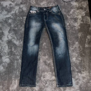Rock revival jeans  - Tvär feta jeans med riktigt tuff fade, storlek W 33 L 32. Byxorna är ifrån rock revival å har massa tuffa detaljer. White stitch och feta knappar och mer. Byxorna är använda så har lite brister. Skriv för bilder på bristerna. 