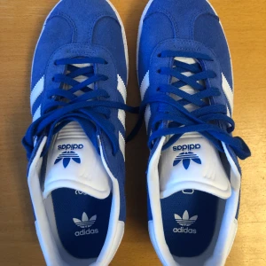 Blå Adidas skor oanvända - Säljer mina blå adidas-skor modell Gazelle storlek 38 1/2. Helt oanvända. Nypris 950:- nu 650 kr. Skickas via post, 650 kr + kostnad för porto. Priset är förhandlingsbart vid snabb affär.