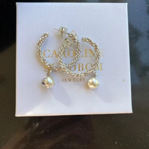 Caroline Svedbom örhängen - Jättefina oanvända örhängen från Caroline Svedbom, kartong medföljer! De här örhängena är tillverkade i en twistad form och har en vita Swarovskipärlor.  Storlek: 44 x 55 mm,  Nypris: 795 kr Modell: Elena Earring Pearls  Priset kan diskuteras