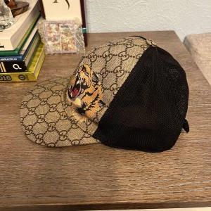 Äkta gucci tiger beige keps storlek S - Äkta Gucci keps beige med tiger på storlek S. Skick är 7/10 pågrund av skador. Säljs pågrund av ingen användning av den längre. Köpt på Guccis hemsida , kvitto tillkommer men utan box. 