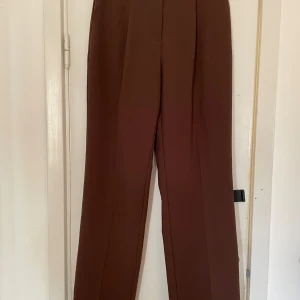 Kostymbyxor från NA-KD - Bruna kostymbyxor från NA-KD Två fickor fram och dekorativa fickor bak. Stl 38 Hög midja och breda ben  En av hämporna har släppt lite bak (se sista bilden) inte trasig men liksom inte ”nedsydd” längre.
