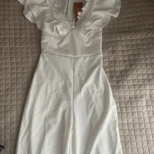 Jumpsuit - Vit jumpsuit med spetsdetaljer vid halsringningen. Jumpsuiten har en V-ringning och en dragkedja i ryggen. Den är ny och oanvänt.  Priset kan diskuteras<3