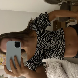 Zebramönstrad offshoulder topp - Säljer en trendig zebramönstrad offshoulder topp med korta ärmar. Toppen är croppad och har en snygg passform som framhäver midjan. Perfekt för en utekväll eller en dag på stan. toppen har inga effekter och är helt i nyskick. Den passar alla från XS till medium eftersom att den är väldigt stretchsigg